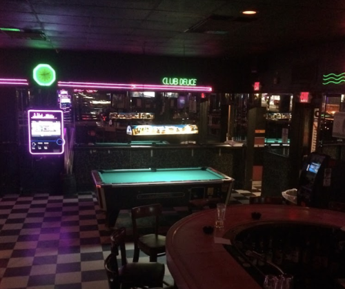 A dimly lit bar with neon lights, a pool table, and a jukebox, creating a retro atmosphere.