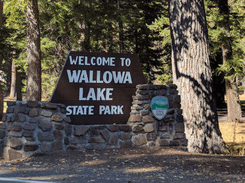 Sign welcoming visitors to Wallowa Lake State Park, surrounded by trees and natural scenery.