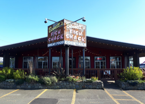 Exterior of Bennett's Fish Shack, featuring a sign and outdoor seating, surrounded by greenery and string lights.