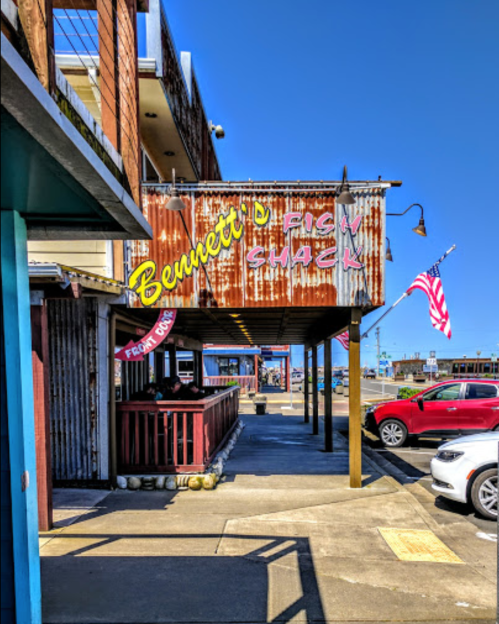 A rustic seafood restaurant sign, "Bennett's Fish Shack," with an American flag nearby and a clear blue sky above.