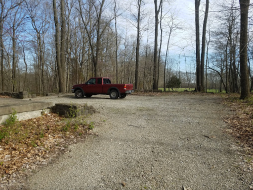 A red pickup truck parked on a gravel area surrounded by trees and a clear blue sky.