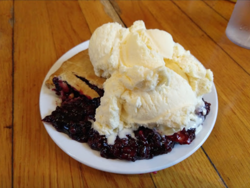 A plate with a slice of pie topped with blueberry filling and a generous scoop of vanilla ice cream.