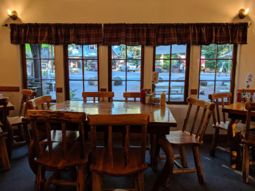 A cozy dining area with wooden tables and chairs, featuring large windows overlooking a street.