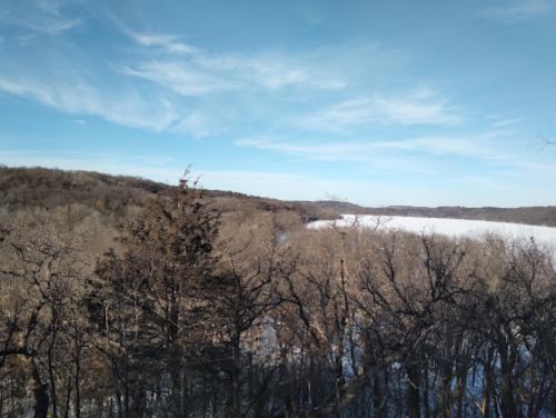 A winter landscape featuring bare trees and a frozen river under a clear blue sky.