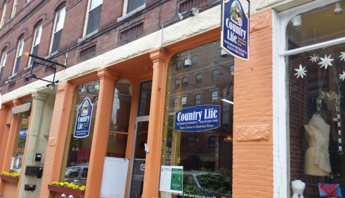 Storefront of "Country Life" with orange pillars and large signs, featuring a window display and nearby street view.