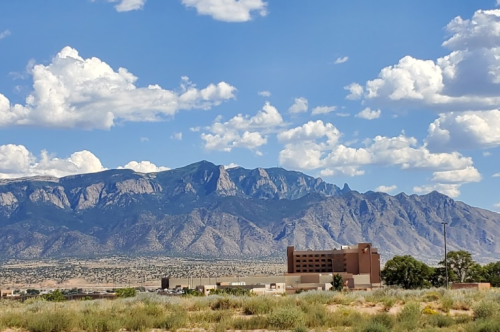 A scenic view of mountains under a blue sky with clouds, featuring a building in the foreground.
