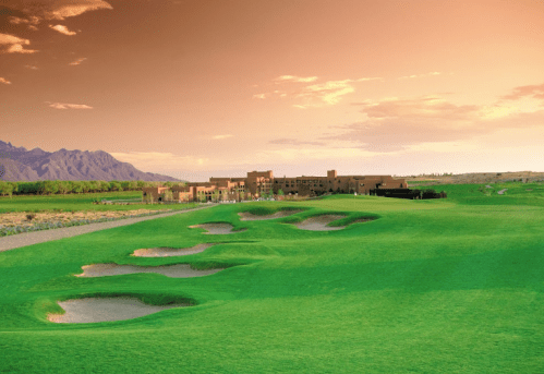 A scenic golf course at sunset, featuring sand traps and mountains in the background.