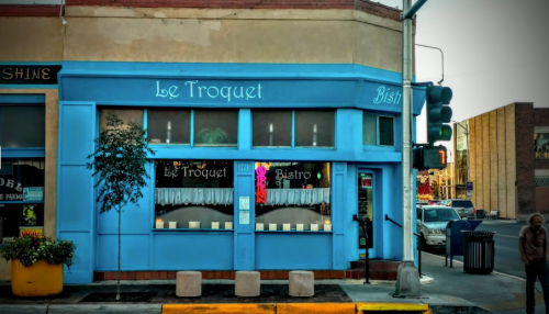 Bright blue exterior of "Le Troquet Bistro" with large windows and a neon sign, located on a street corner.