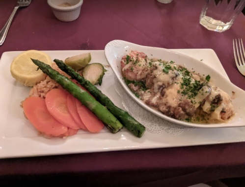 A plate of seafood with cheese, served with asparagus, carrots, Brussels sprouts, and a side of rice.