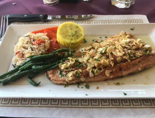 A plated meal featuring salmon topped with almonds, rice, green beans, and a lemon slice on a decorative white dish.