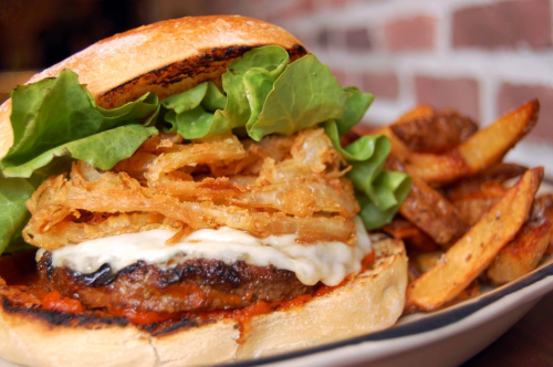 A close-up of a burger with lettuce, crispy onions, and sauce, served with golden-brown fries on the side.