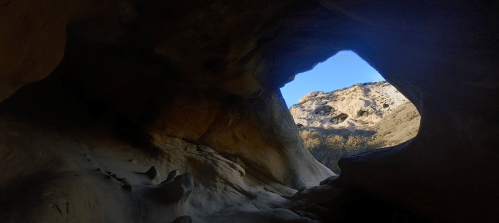 View from inside a cave, showing a bright opening with a glimpse of the landscape outside against a clear blue sky.