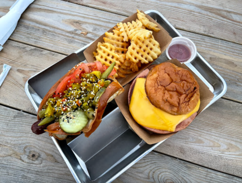 A tray with a sandwich topped with cheese and vegetables, waffle fries, and a small cup of dipping sauce.