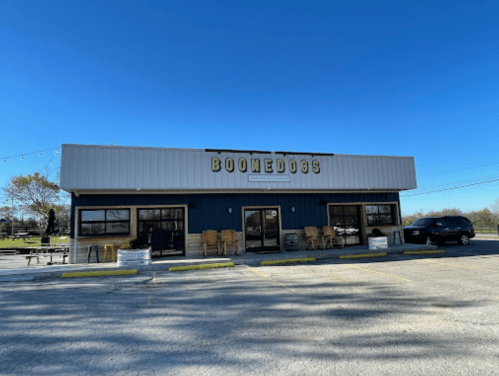 A modern building with the sign "Boomedogs," featuring outdoor seating and a clear blue sky.