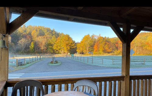 A scenic view from a porch, showing a road winding through trees with autumn colors and a clear blue sky.