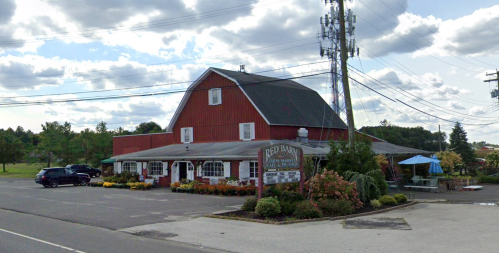 Red Barn restaurant with a red barn-style exterior, surrounded by greenery and a parking lot under a cloudy sky.