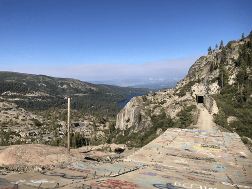 A scenic view of a mountainous landscape with a lake, featuring a graffiti-covered concrete surface in the foreground.