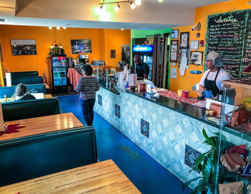 A colorful café interior with a counter, seating areas, and customers interacting with staff.