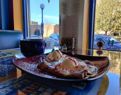A plate of dessert with ice cream and sauce, next to a cup of tea, with a sunny street view outside the window.