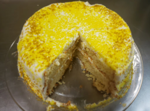 A round cake with yellow frosting and a slice cut out, revealing layers inside.