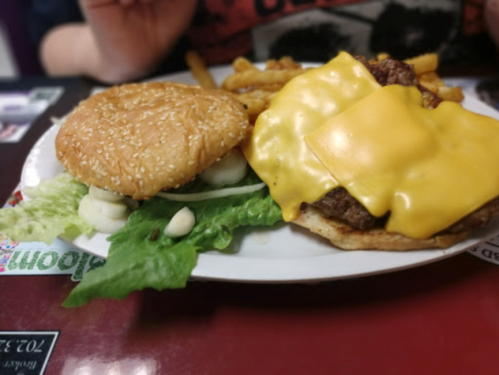 A plate with a sesame seed bun, lettuce, and a cheeseburger topped with two slices of melted cheese and fries.