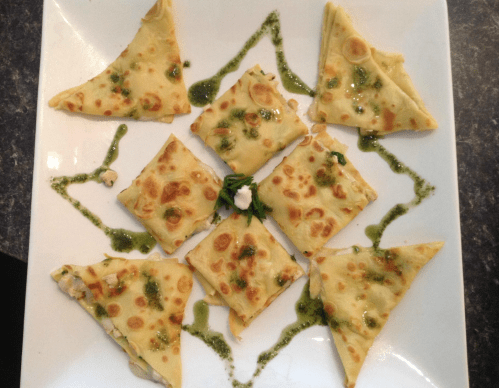 A plate of triangular pieces of crepes drizzled with green sauce, arranged in a star pattern.