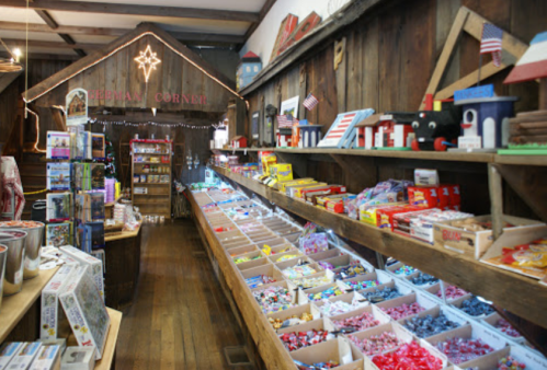 A cozy candy shop with wooden shelves filled with colorful candies and treats, decorated with festive lights and flags.