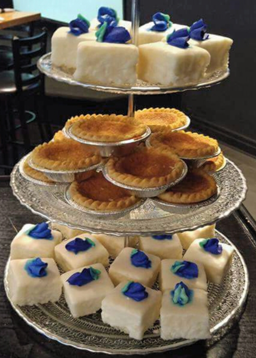 A tiered dessert display featuring white cakes with blue flowers and small tart shells.