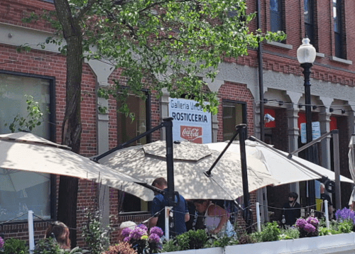 Outdoor dining area with umbrellas, plants, and a sign for "Galleria Umberto Rosticceria" in a brick building setting.