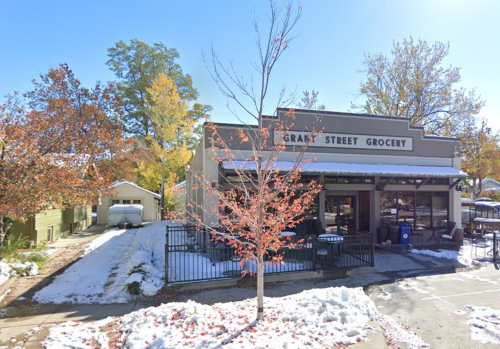 A grocery store with a sign reading "Grant Street Grocery," surrounded by autumn trees and light snow on the ground.