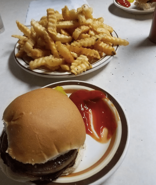 A plate with a hamburger and ketchup, alongside a plate of crinkle-cut fries.