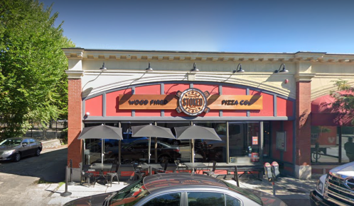 Exterior of a pizza restaurant with a sign reading "Wood Fired Pizza Co." and outdoor seating under umbrellas.