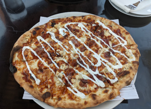 A freshly baked pizza topped with barbecue sauce, chicken, and drizzled with white sauce, served on a round plate.