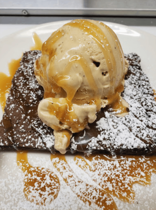 A warm brownie topped with a scoop of vanilla ice cream and drizzled with caramel sauce, dusted with powdered sugar.