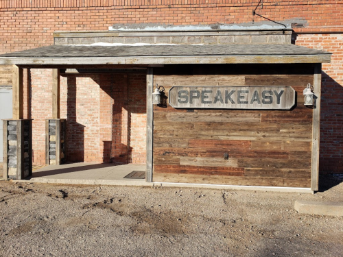 A rustic wooden entrance with a sign reading "SPEAKEASY," set against a brick wall.