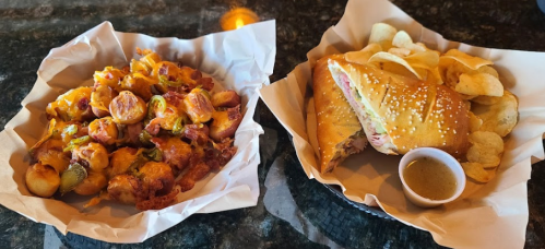 A basket of loaded nachos with toppings and a sandwich with chips and dipping sauce on the side.