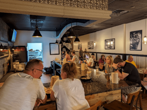 A busy restaurant interior with patrons seated at a long bar, enjoying food and drinks in a casual atmosphere.