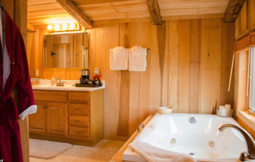 Cozy wooden bathroom featuring a jacuzzi, vanity, and a red robe hanging on the door. Soft lighting enhances the warmth.