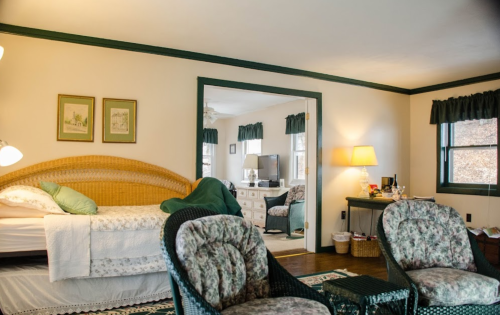 Cozy bedroom with a wicker bed, two floral chairs, and a mirror reflecting a bright, inviting space.