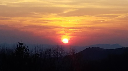 A vibrant sunset over rolling hills, with orange and pink hues illuminating the sky.