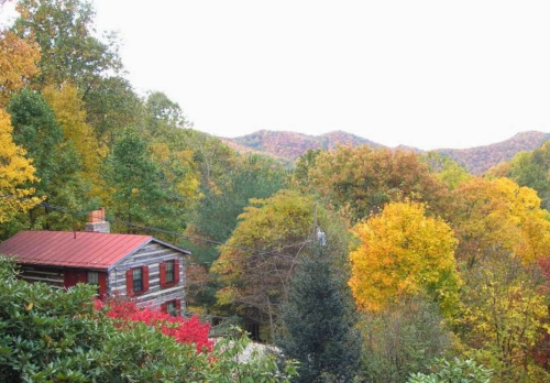 A rustic cabin surrounded by vibrant autumn foliage and mountains in the background.