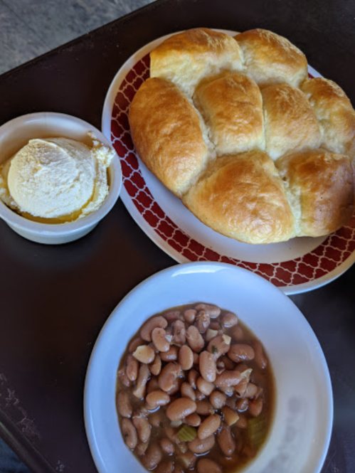 A plate with fluffy rolls, a bowl of pinto beans, and a small dish of butter or ice cream.
