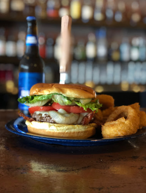 A juicy burger with lettuce, tomato, and onion rings, served with a beer in a bar setting.