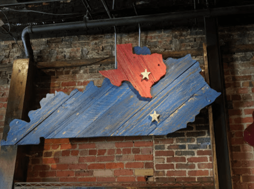 Wooden wall art depicting the shapes of Texas and Kentucky, painted in red, blue, and featuring two white stars.