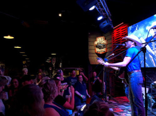 A country musician performs on stage in a lively bar, with an engaged audience enjoying the show.