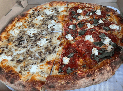 A pizza box containing two halves: one with mushrooms and cheese, the other with tomato, herbs, and dollops of cheese.