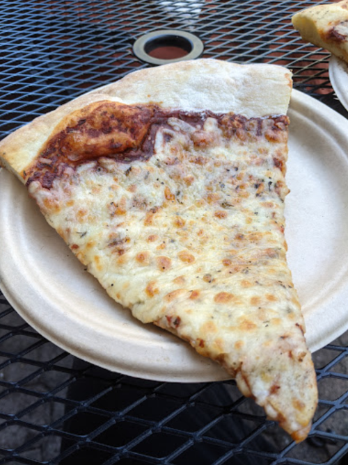 A slice of cheese pizza on a paper plate, resting on a black metal table.