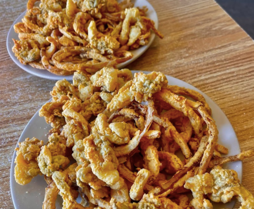 Two plates of crispy fried onion rings and calamari on a wooden table.