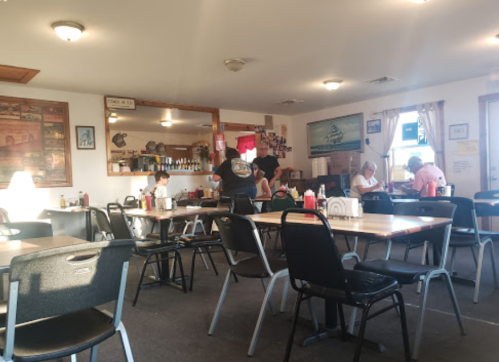 A cozy diner interior with tables, chairs, and patrons enjoying their meals. A server attends to customers.