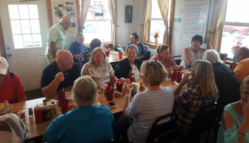 A busy restaurant scene with a diverse group of people dining and chatting around tables filled with condiments.